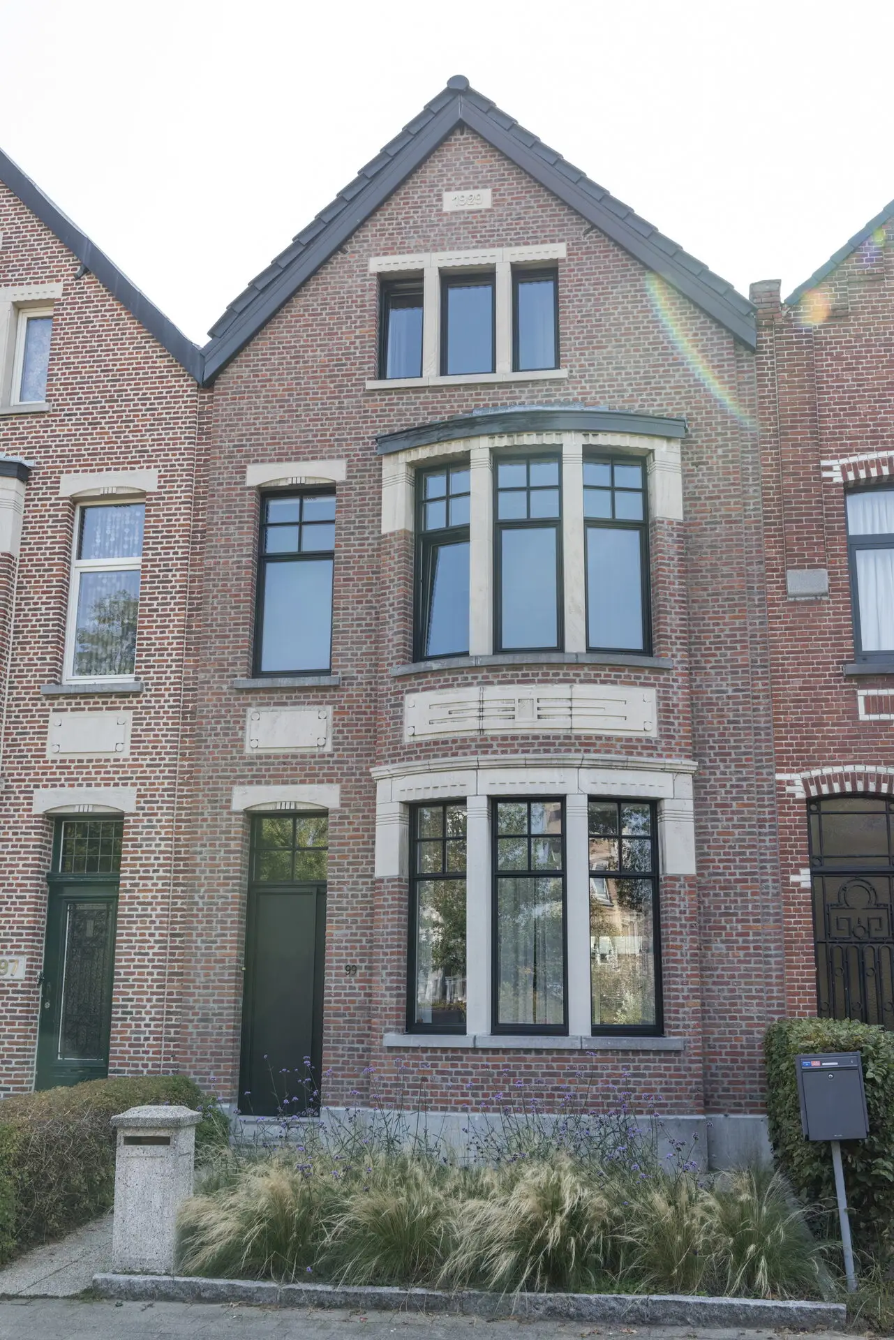 Moderne voorgevel met antracietgrijze raamprofielen en een strakke aluminium voordeur in Schoten.